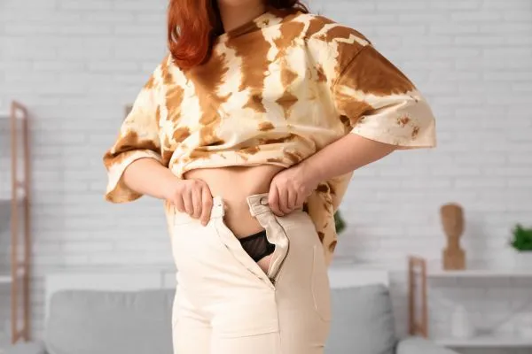 Image of woman trying to do her trousers up after pregnancy weight gain Stratford
