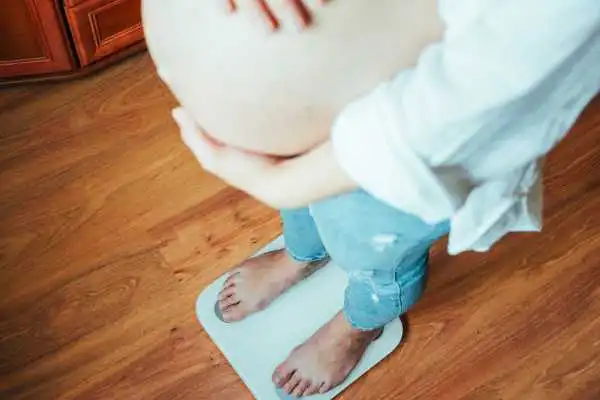 Image of woman weighing herself and experiencing weight gain through pregnancy Stratford